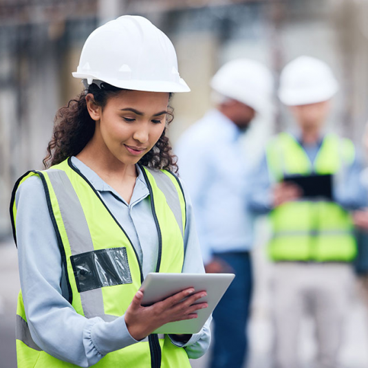 Schneller Einstieg in das digitale Materialmanagement Frau nimmt Material auf Baustelle per App entgegen. Sie trägt eine gelbe Warnweste und einen weißen Helm.