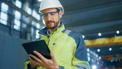 Die digitale Supply Chain: Mann auf Baustelle mit Helm und gelber Warnweste hält ein Tablet.